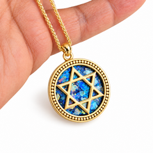 A gold pendant necklace set with Roman glass inlay and a gold Star of David, held in a person's hand against a white background.