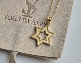 Gold star-shaped pendant on a chain with 'Yoels Jewelry' card in the background