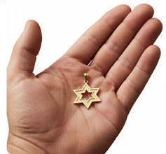 Gold star-shaped pendant held in a hand on a white background