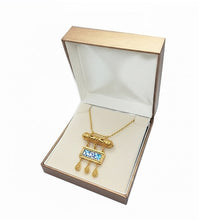Gold necklace with a blue pendant in an open jewelry box on a white background
