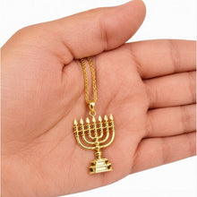 Gold menorah pendant on a chain held in a hand against a white background
