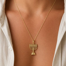 Gold menorah pendant necklace on a person wearing a white shirt.