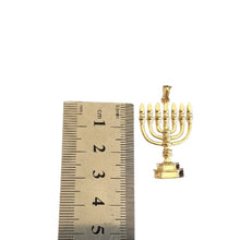 Gold menorah pendant next to a ruler for scale on a white background