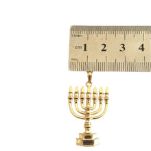 Gold menorah pendant with a ruler for scale on a white background