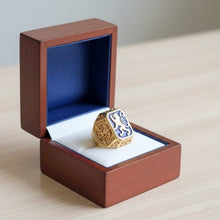 Gold ring with blue gemstone in an open wooden box on a light surface.