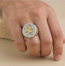 Gold and silver lion emblem ring on a hand against a beige background