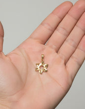 Gold Star of David pendant held in a hand against a neutral background