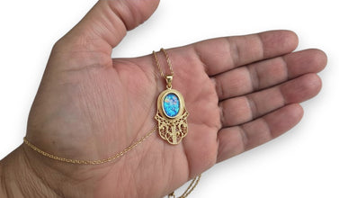 Gold necklace with a pendant featuring blue opal stone held in a hand against a white background