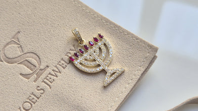 Gold menorah pendant with red stones on a Soels Jewelry branded card.