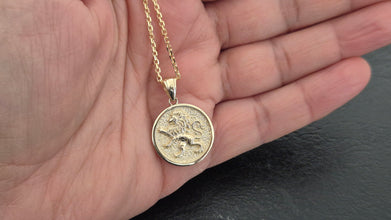 Gold  llion of Judah necklace with a round pendant held in a hand against a dark background