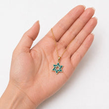 Hand holding a gold necklace with a star-shaped pendant on a white background