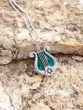 Silver lyre-shaped pendant with green stone on a stone surface