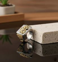 Silver and gold ring on a textured surface with a blurred background