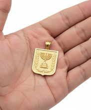 Gold pendant with Menorah design held in a hand against a white background