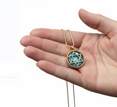 Gold necklace with a blue gemstone pendant held in a hand against a white background