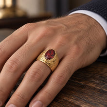 A close-up of a hand wearing a gold signet-style ring with a large oval red gemstone, resting on a dark wooden surface.