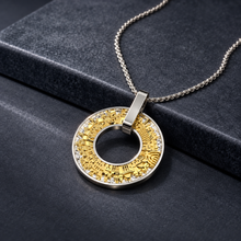 Jerusalem pendant with yellow gold city design, silver frame and sparkling stones on a black rock surface