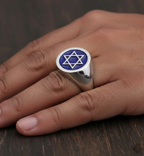 Silver ring with a blue stone and star design on a hand against a wooden background