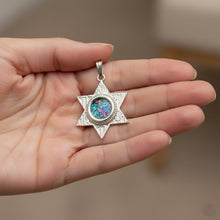 Silver Star of David pendant with colorful stone held in a hand against a neutral background