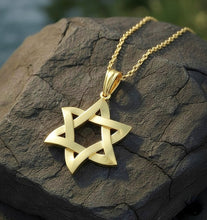 Gold star-shaped pendant on a chain resting on a textured stone surface.