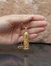 Gold  mezuzah necklace with a detailed pendant held in a hand against a neutral background