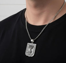 Silver necklace with a pendant worn by a person on a black shirt against a light gray background