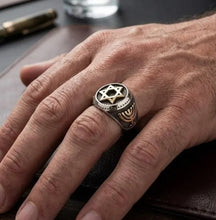 Hand wearing a ring with a Star of David design on a textured surface.