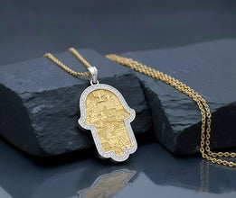 Gold and silver Hamsa pendant on a chain against a dark stone background