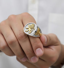 Gold and silver ring with a lion emblem on a person's finger against a white background