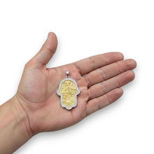 Hand holding a gold Hamsa pendant against a white background