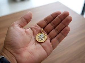 Gold pendant with a lion design held in a hand on a wooden surface