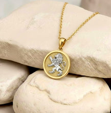 Gold necklace with a lion emblem pendant on a stone surface