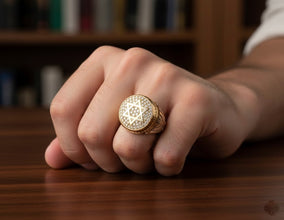 Hand wearing a gold ring with a diamond design on a wooden surface