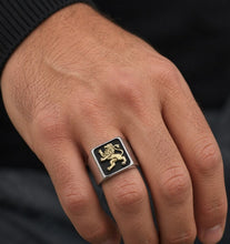 Hand wearing a ring with a lion emblem on a dark background