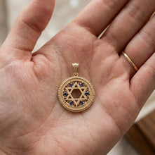 Gold Star of David pendant with blue stones held in a hand.