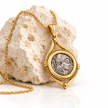 Gold Roman coin pendant leaning against a rock