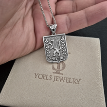 Silver Lion of Judah pendant with chain held in a hand above a Yoels Jewelry suede pouch