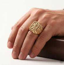 Gold ring with intricate design on a person's finger against a neutral background