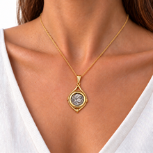 Woman wearing a gold Roman coin pendant with a white V-neck top.