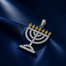 Jewelry pendant resembling a menorah with yellow stones on a blue satin background