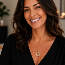 Woman wearing a gold necklace with a circular pendant, smiling indoors.