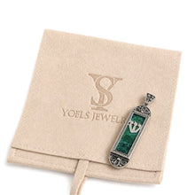 A silver-toned rectangular pendant with a green stone inlay, displayed on a beige velvet jewelry pouch embossed with the YOELS JEWELRY logo.