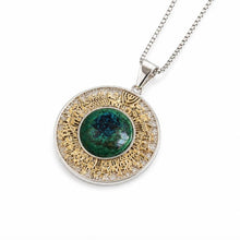 A round pendant necklace featuring a central green stone surrounded by a halo of small clear stones and an outer gold-toned textured ring, suspended from a silver-toned chain on a white background.