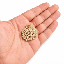 Gold filigree pendant held in a hand on a white background