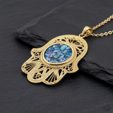 Gold filigree hamsa with roman glass pendant on a dark surface