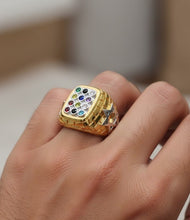 Gold ring with multicolored gemstones on a hand against a neutral background
