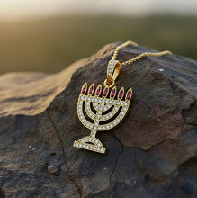 Gold Menorah pendant with red stones on a rocky surface