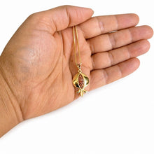 A gold pendant necklace shaped like a pomegranate with red gemstone accents, displayed on an open hand against a white background.
