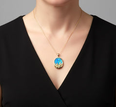 Woman wearing a black dress with a gold necklace featuring a blue pendant.