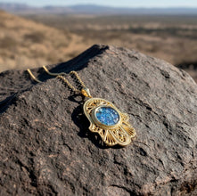 Gold necklace with a blue pendant on a rocky surface